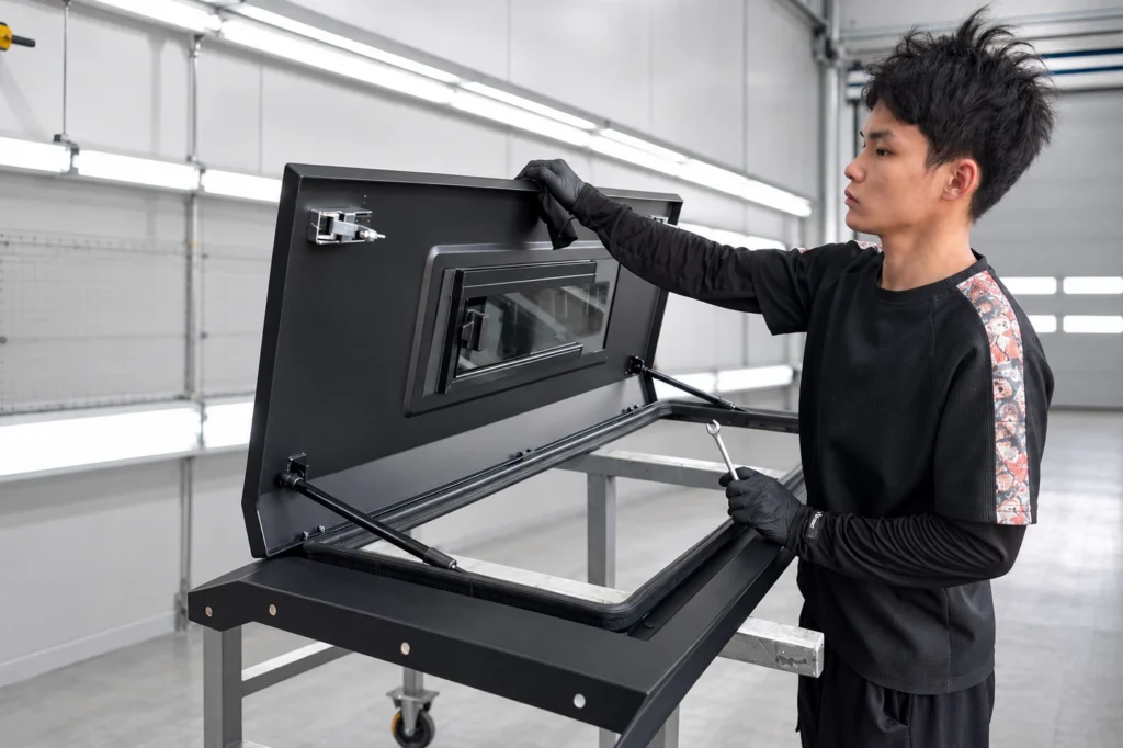 offroadcap-process-08-final-inspection-v2.webp Worker inspecting an open pickup canopy door, window, weather seal and gas struts before delivery